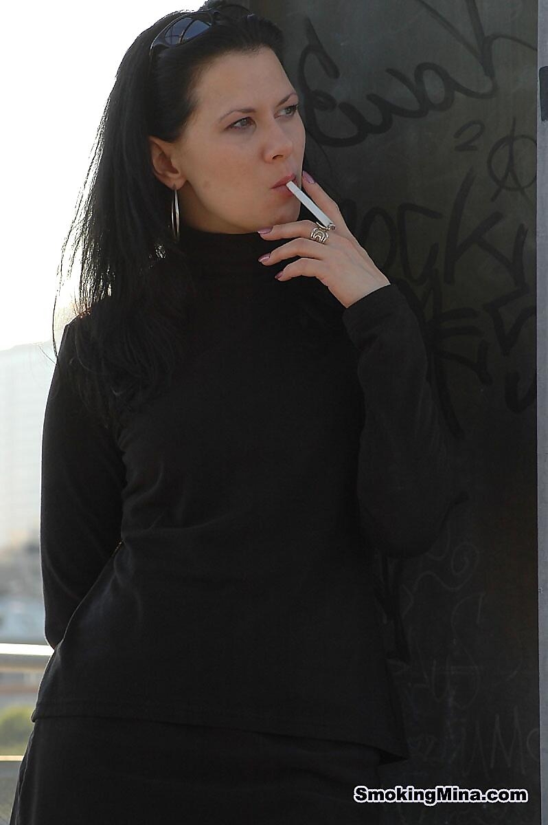 Fully clothed brunette lights up a cigarette with her sunglasses atop her head